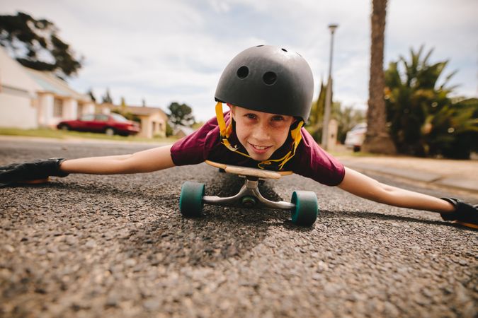 Boy with helmet lying on his skateboard outdoors on road