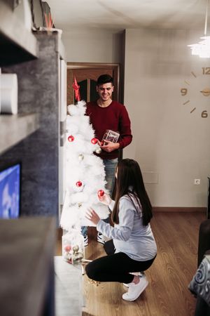 Young couple expecting baby arranging Christmas tree at home