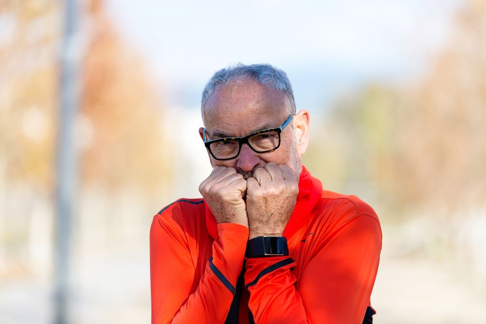 Older male warming his fingers to his mouth while outside
