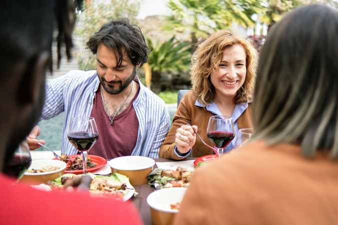 A group of friends share a warm, intimate meal outdoors, enjoying wine and engaging in cheerful conversation