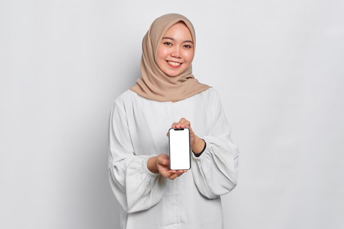 Asian Muslim woman presenting cell phone with mockup screen