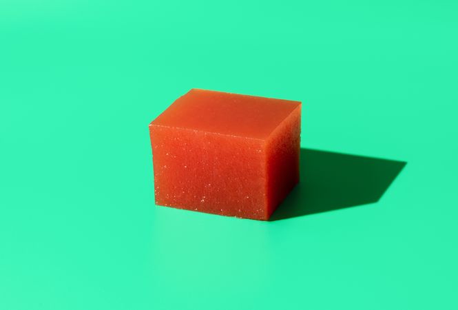 Cube of quince jelly for cheese plate on bright green background