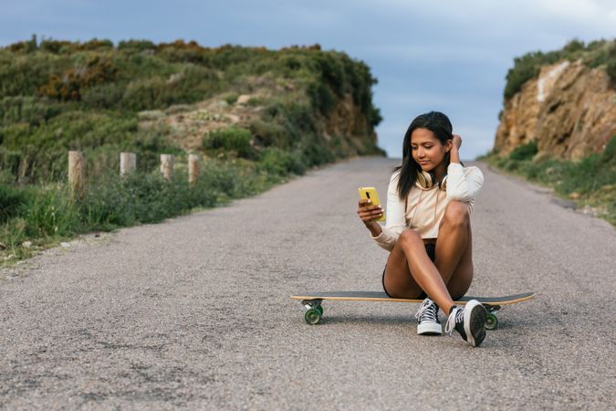 Cheerful woman using mobile phone while sitting on longboard