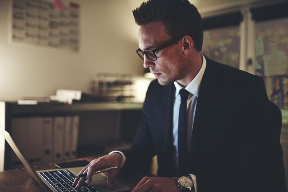 Man in suit and glasses working on his laptop at night