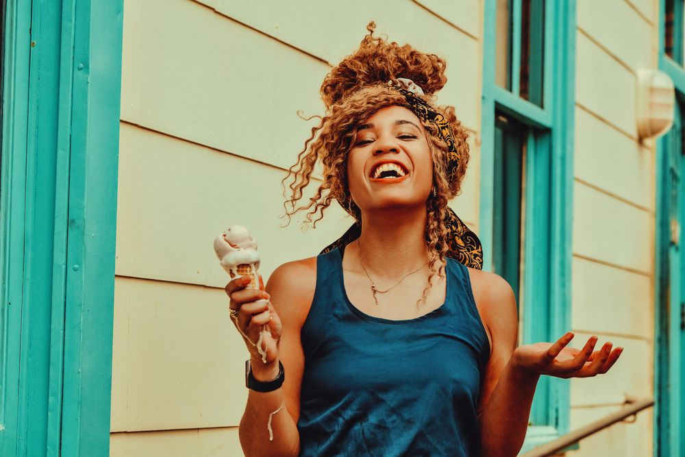 Expressive Black female snacking on an ice cream cone in the sun