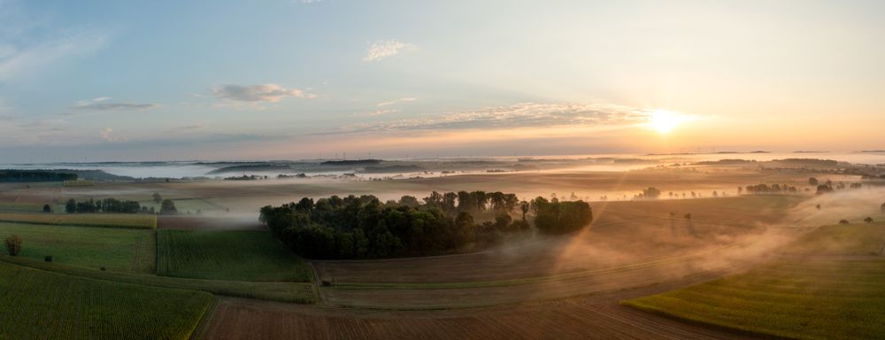 Drone scenery at golden hour with agricultural fields and rolling hills enlightened by sunrise