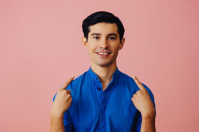 Smiling Latino man in pink studio looking up and pointing both fingers at his face