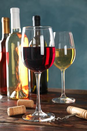 Corkscrew, bottles and glasses with wine on wooden table against blue background