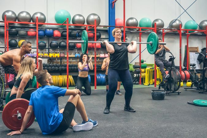 Proud woman lifting weights while her gym mates cheering her on