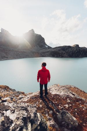 Back view of man in red jacket standing on waterside of frozen lake in Switzerland