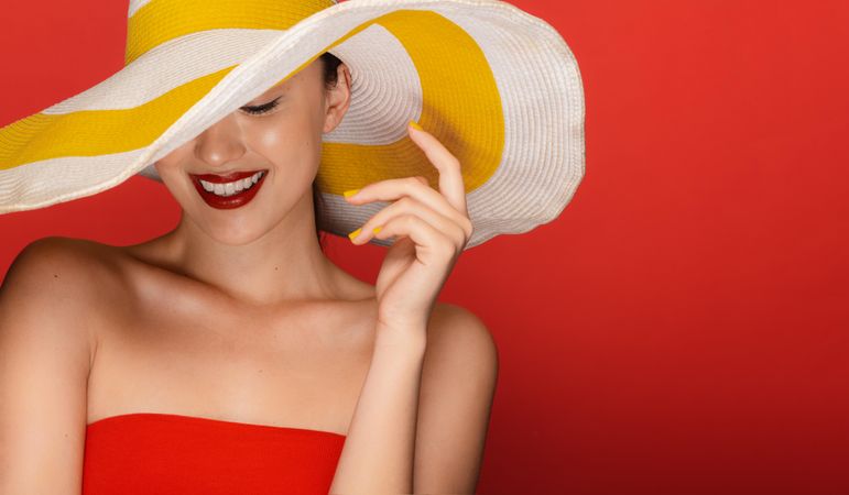 Happy young female wearing summer hat in red studio