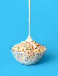 Pouring mayo over oliveir salad, minimalist on a blue background