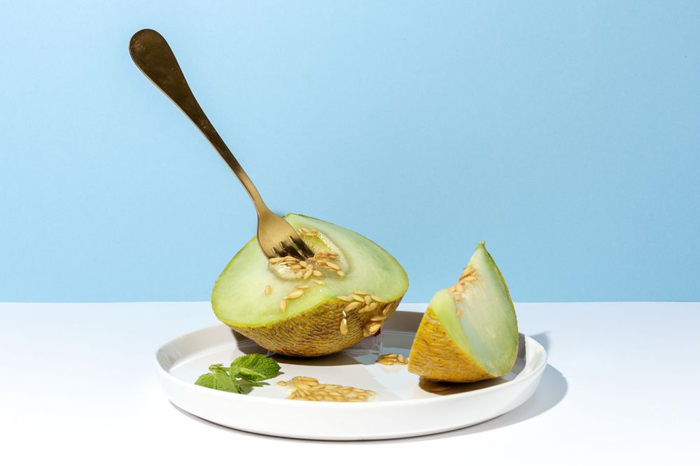 Sliced small melon on plate with spoon and fork