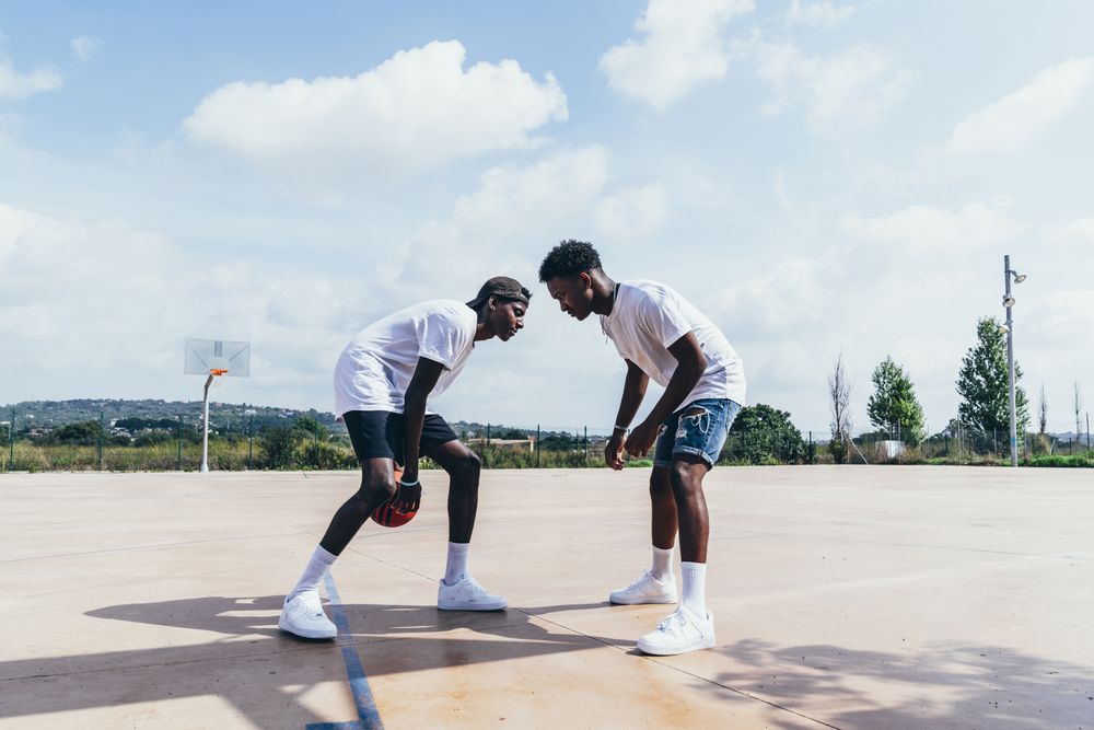 2 Black men playing basketball in bright day