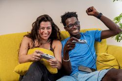 Excited diverse couple celebrating a victory while playing video games at home, with the man making a winning gesture.