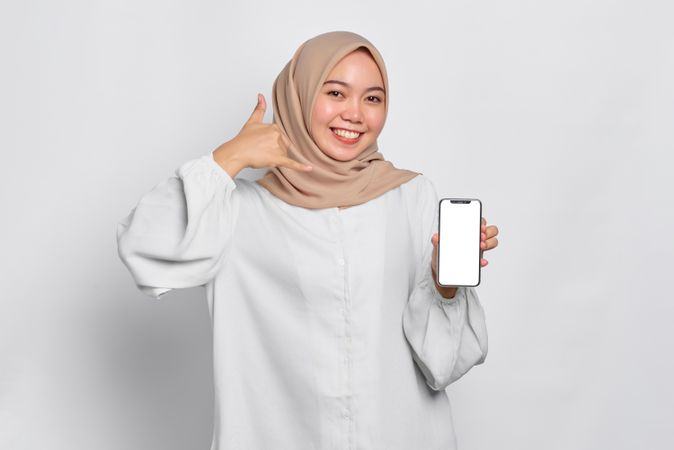 Asian Muslim woman presenting cell phone with mockup screen and hand making phone shape