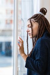 Pensive woman with dreadlocks looking out the window