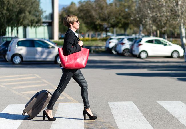 Female walking confidently across street with roller suitcase behind her
