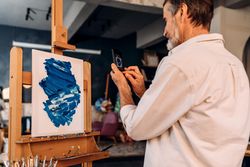 Older male artist taking picture of easel with smartphone