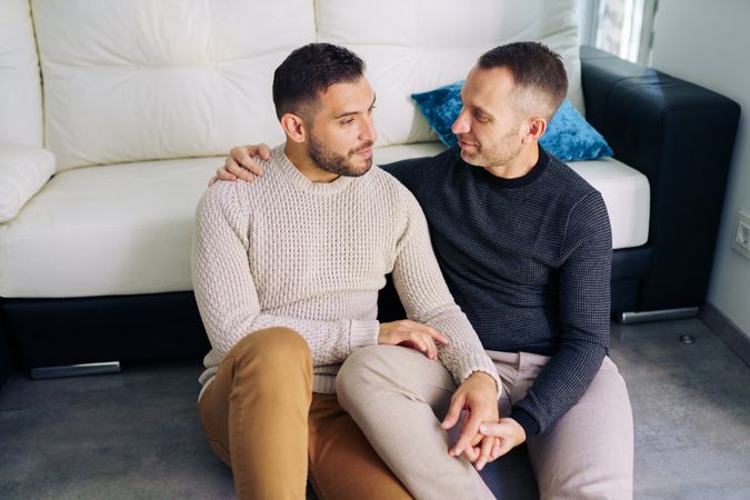 Cute male couple holding each other while sitting on floor at home