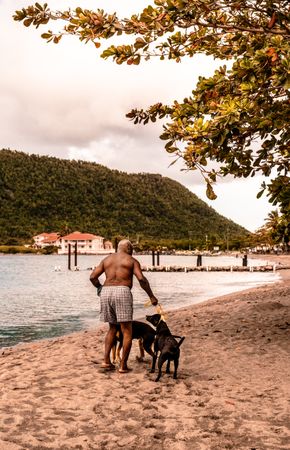 Back view of topless older man with two dog standing by shoreline in Dominican Republic