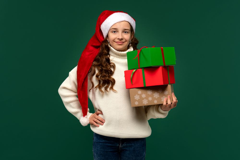 Girl in Santa hat holding stack of wrapped Christmas presents.