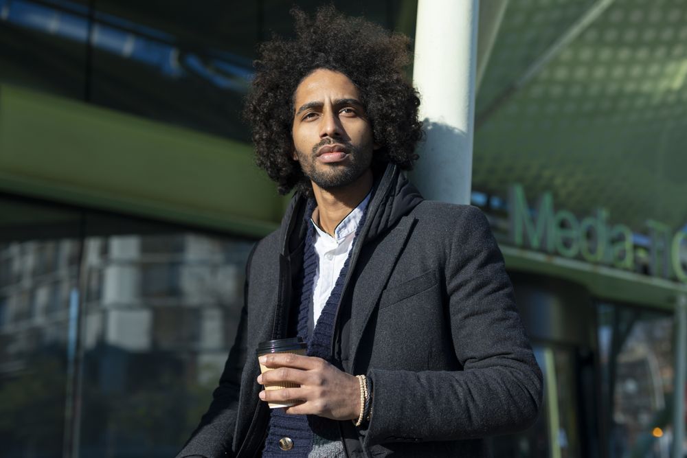 Portrait of Black man in jacket standing outside of building holding warm beverage