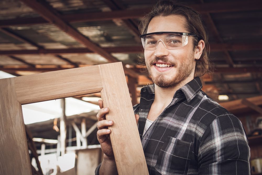 Smiling male woodworker proudly holding wooden frame he made in his workshop
