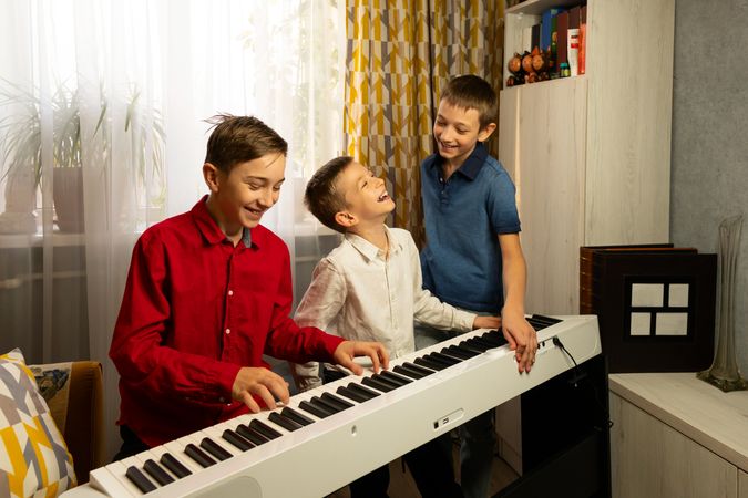 Three boys laughing and playing the piano together