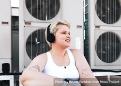 Woman with tattoos, smart watch and headphones smiling in front of fans on rooftop 4dmwAb