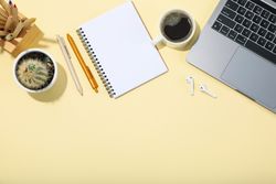 Top view of laptop, notebook, pens, coffee, cactus, earbuds with copy space