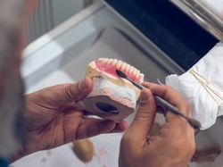 Crop dentist technician applying steel spatula on jaw implants