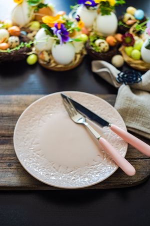 Easter holiday table setting with delicate pink plate surrounded by decorative eggs and colorful flowers