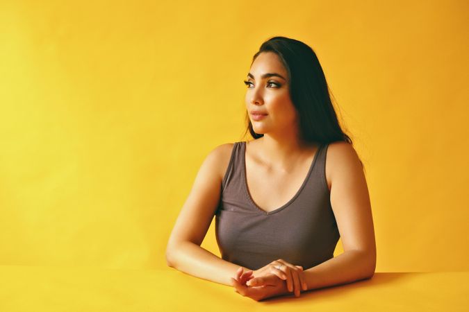 Pensive Hispanic woman looking wistfully away from camera and sitting in yellow room, copy space