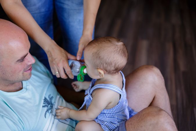 Crop mother giving water to baby on father lap