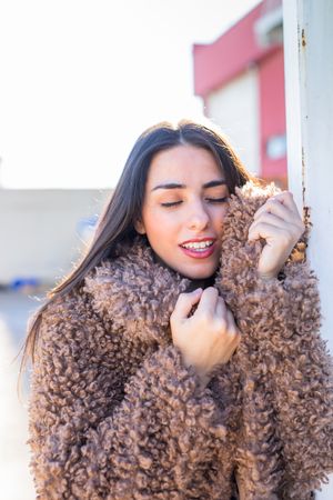 Cheerful woman wrapping in coat on street