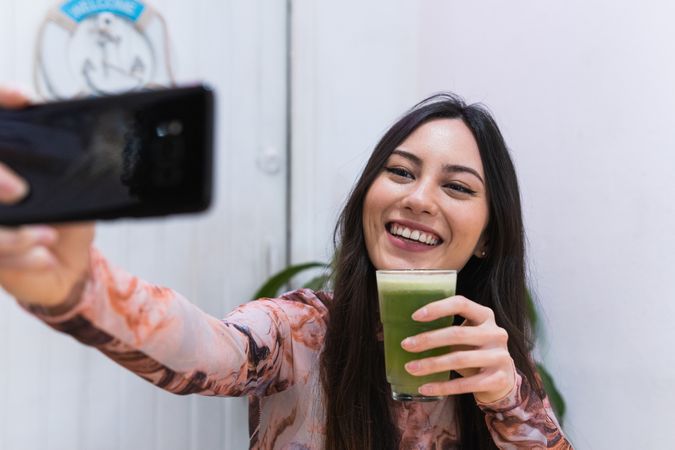 Smiling woman taking self portrait on smartphone at table in bar