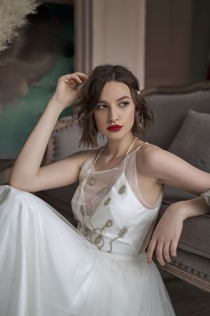 woman with red lips in white dress looking away while sitting on floor beside sofa