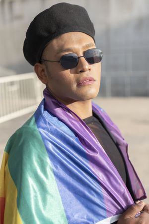 Gay man with make up on under LGBT rainbow flag while looking at camera. Concept of Pride. Pride month.