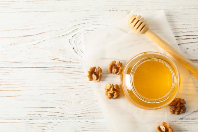 Walnuts, dipper, parchment and glass jar with honey on neutral background, top view