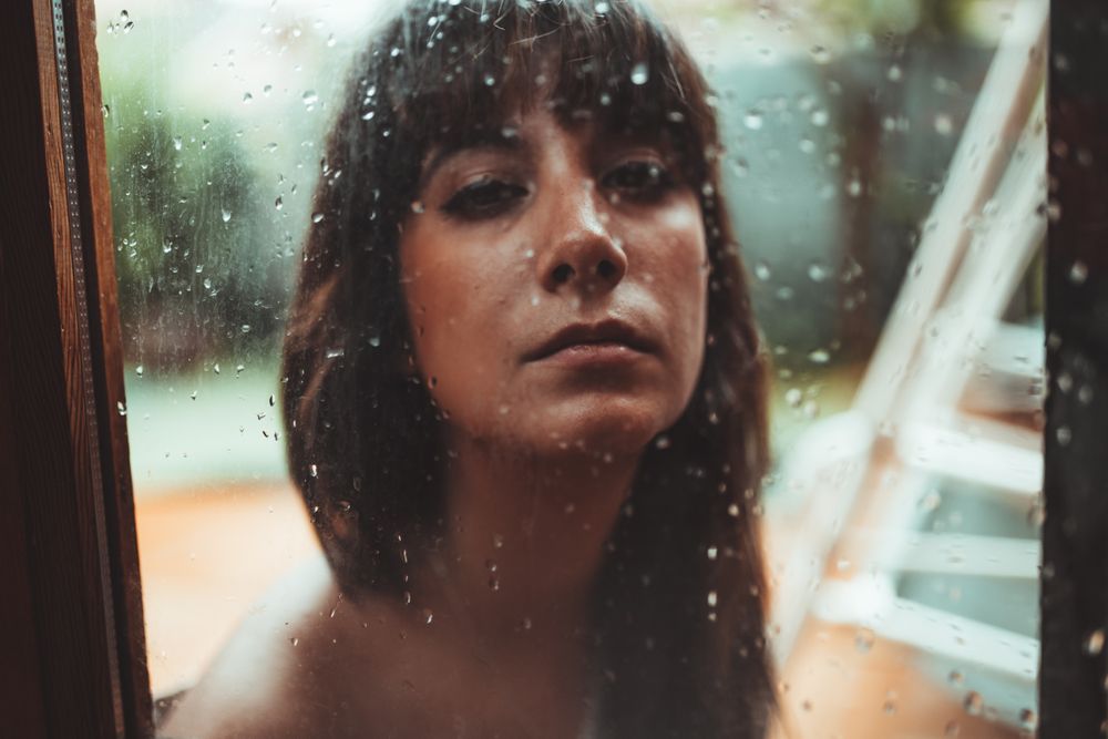 Woman looking at camera behind a wet glass