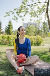 Smiling young woman sitting on exercise mat and holding ball