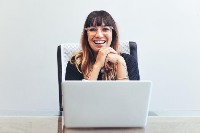 Close up of a smiling woman sitting at her desk in office with a laptop in front