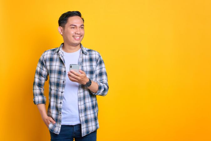 Smiling Asian male looking down at his phone in studio shoot with copy space