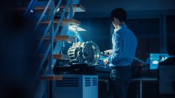 Professional Automotive Engineer in Glasses is Working on Transmission Gears in a High Tech Innovative Laboratory with a Computer Screens.