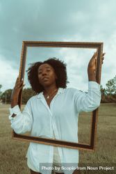 Portrait of Black woman in light shirt holding brown wooden frame 42xrd0