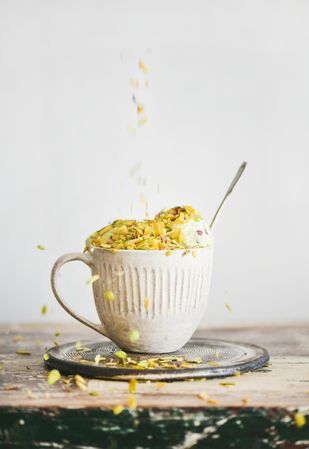 Cup of ice cream being topped with pistachio nuts on light background
