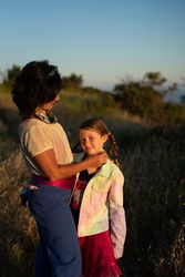 Young girl outside in canyon smiling at camera with her mother touching her face