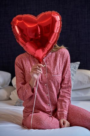 Young woman hiding face behind red heart balloon