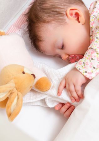 Baby girl sleeping in a cot with pacifier and toy